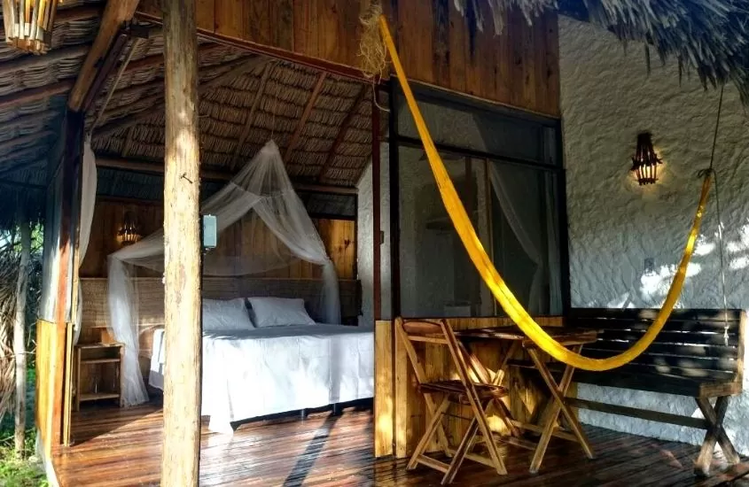 cama de casal, cadeiras e mesa de madeira em bangalô de vila junco, um dos melhores hotéis em santo amaro