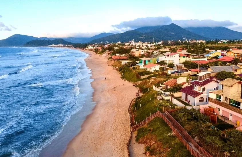 vista aérea de montanhas e casas em frente a praia, durante o dia, em Campeche, uma ótima área onde ficar em Florianópolis