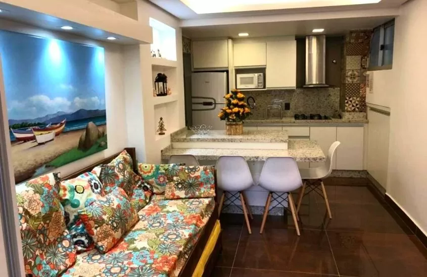 sofá, mesa, cadeiras e geladeira em Suítes Jurerê Internacional, uma casa de temporada em florianópolis