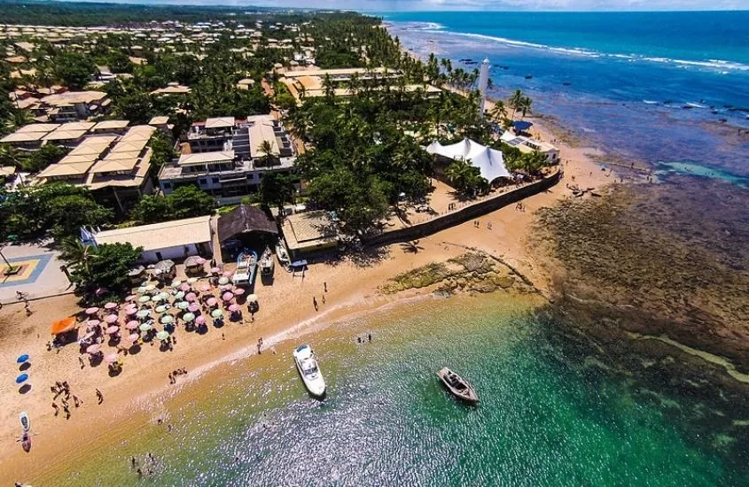 vista aérea, durante o dia, de barcos em mar, pessoas na areia e construções cercadas de árvores em Praia do Forte na Bahia, um dos melhores destinos para viagem em família no brasil