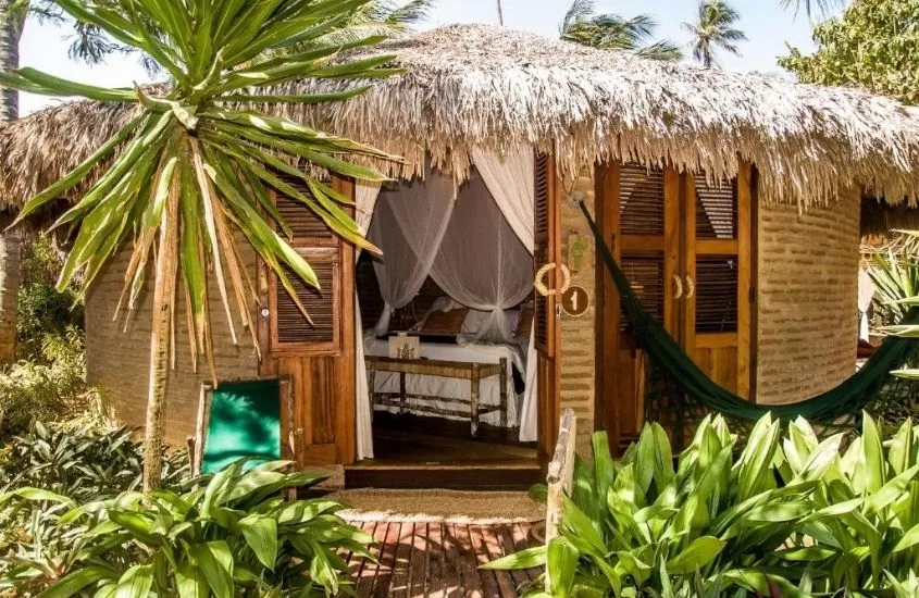cama de casal em chalé rodeado por árvores, com varanda onde há uma rede de descanso em Pousada Vila Kalango, um dos melhores hotéis do nordeste