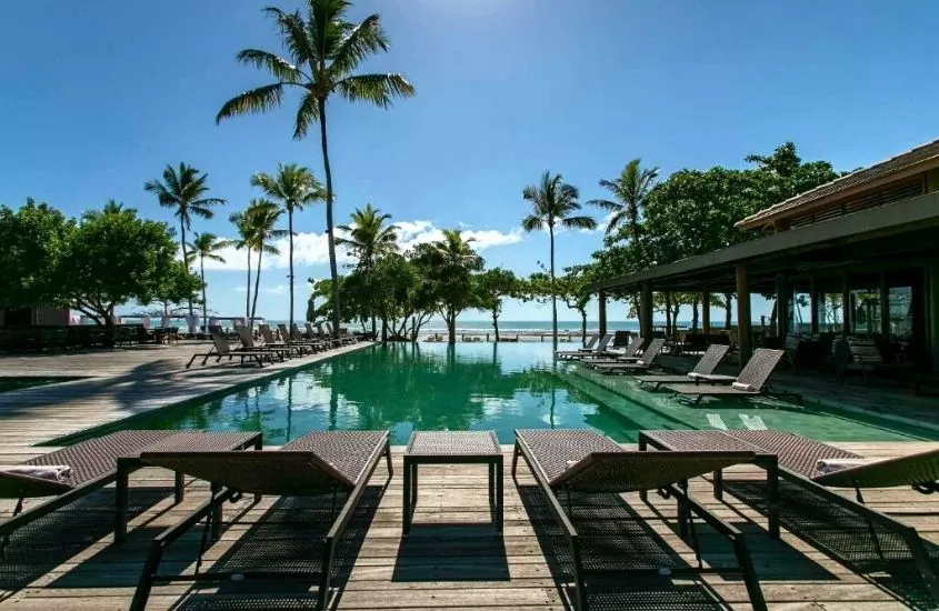espreguiçadeiras e coqueiros ao redor de piscina com vista para o mar, durante dia ensolarado em área de lazer de kuara hotel, um dos melhores hotéis pé na areia do nordeste