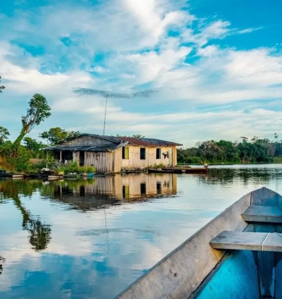 canoa em rio, passa em frente a casa cercada de árvores, durante o dia em Amazônia