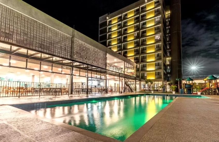 piscina iluminada, durante a noite, em área de lazer externa de WAM Solar Pedra da Ilha um hotel perto do beto carrero world