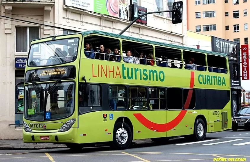 ônibus verde de linha de turismo, cheio de pessoas, passa em avenida, durante o dia