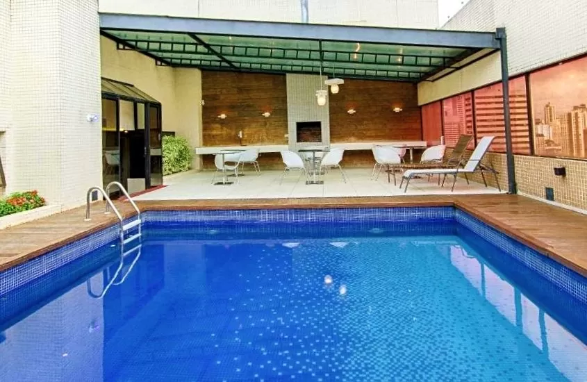 piscina, espreguiçadeiras e cadeiras em área de lazer de victória villa curitiba, um dos melhores hoteis em curitiba