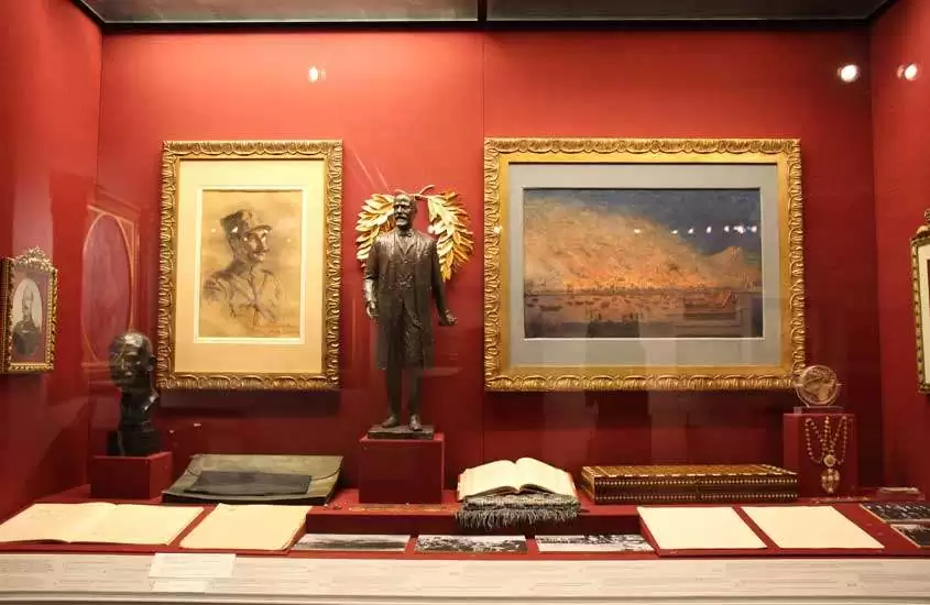 Interior de um museu com paredes vermelhas, quadros, estátuas e itens históricos