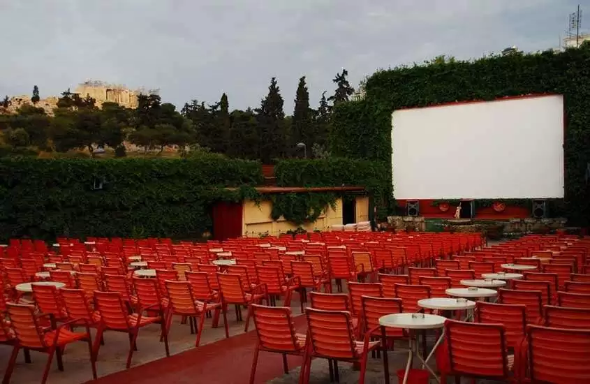 Em um fim de tarde, cinema ao ar livre com cadeiras, telão, plantas e árvores ao redor