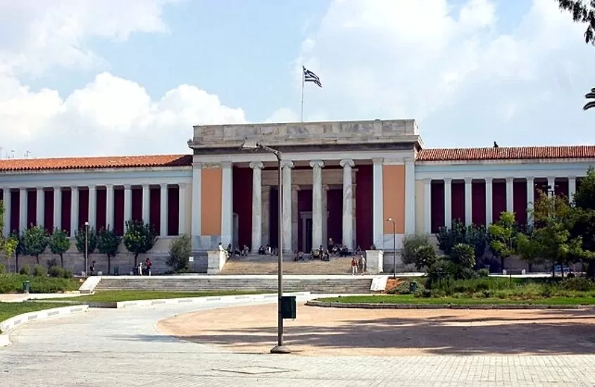 árvores em frente a construção rosa com colunas de mármore, onde funciona o Museu Arqueológico Nacional de Atenas