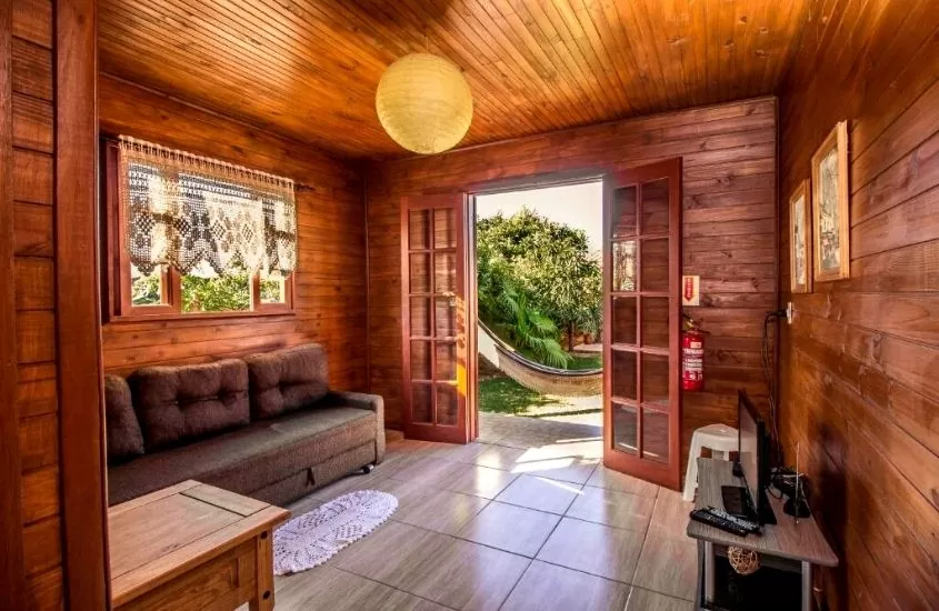sofá, mesa e televisão em hospedagem feita de madeira cercada pela natureza da Green Mountain Pousada
