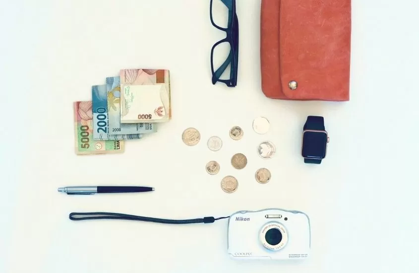 euros, moedas, caneta, câmera, óculos, relógio e carteira vermelha em cima de superfície branca