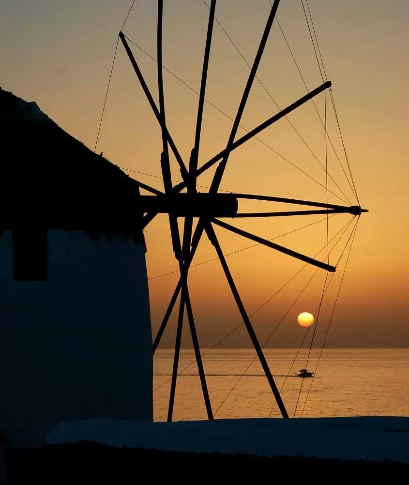 silhueta de moinho de vento e ao fundo, barco em mar, durante o pôr do sol em mykonos