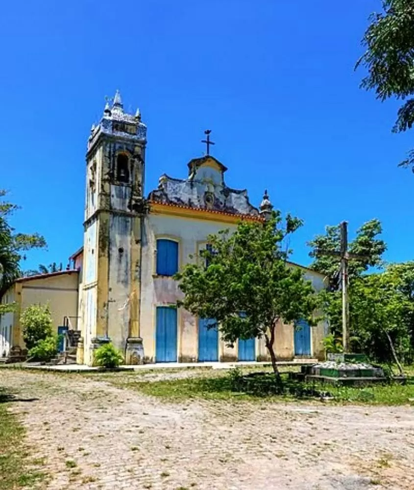 igreja branca com detalhes amarelos e portas azuis, cercada de árvores em dia ensolarado em ilha de itaparica ba