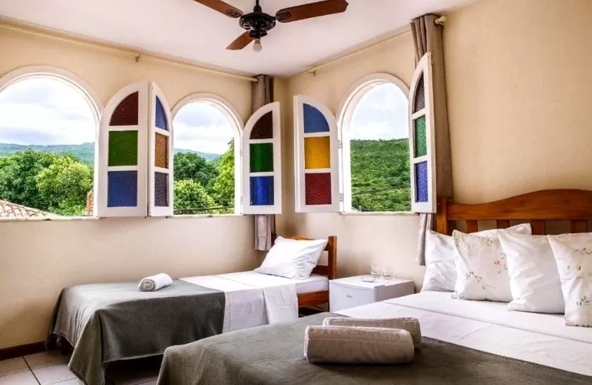 camas de solteiro e casal e janelas abertas com vista para árvores em quarto do Pitaya Rosa Pousada