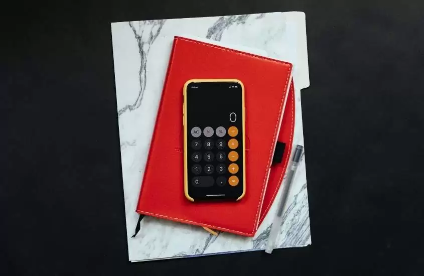 celular com capa amarela, em cima de caderno vermelho, exibe aplicativo de calculadora