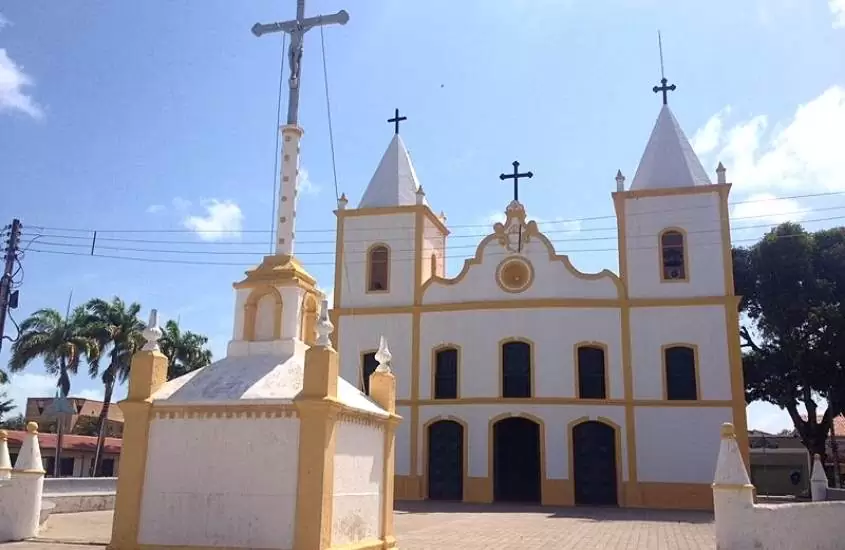 fachada de igreja branca com detalhes amarelos, durante dia ensolarado