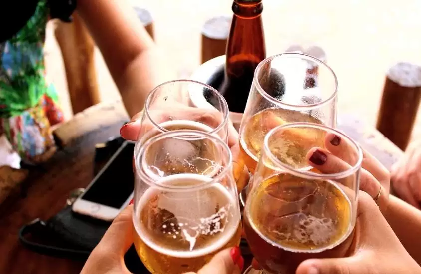 pessoas brindam segurando copos de vidro com cerveja