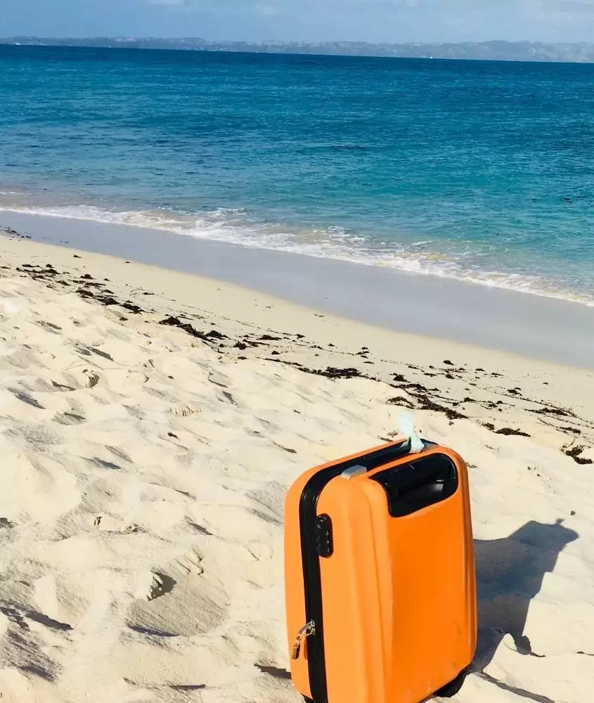 mala de viagem laranja na areia da praia em frente ao mar, durante dia ensolarado