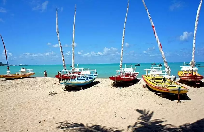 barcos coloridos em areia de praia, durante dia ensolarado em pajuçara, uma região para quem busca onde ficar em Maceió