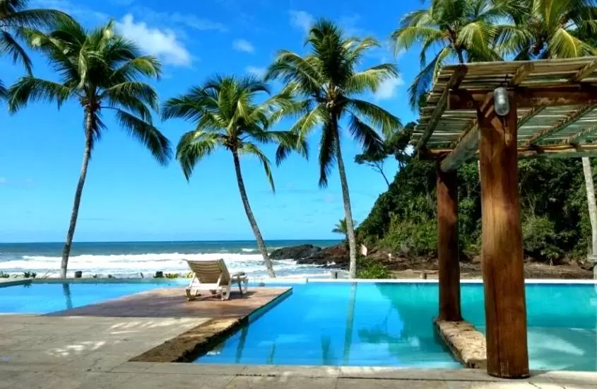 piscina cercada de coqueiros com vista para praia, durante dia ensolarado em área de lazer de São José Beach Club & Residence
