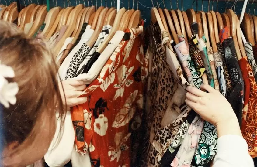 mulher conferindo roupas em cabide de blusas coloridas em loja