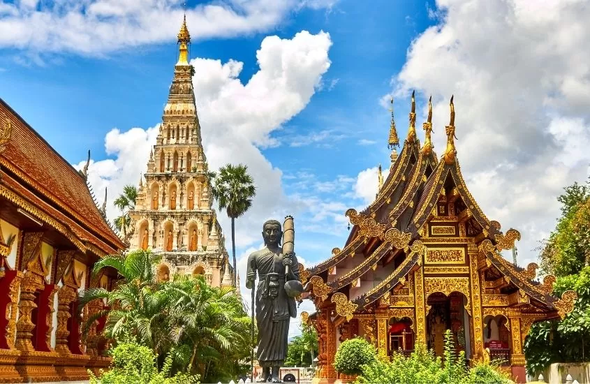 estátua em meio a templos dourados e vermelhos, durante o dia na tailândia