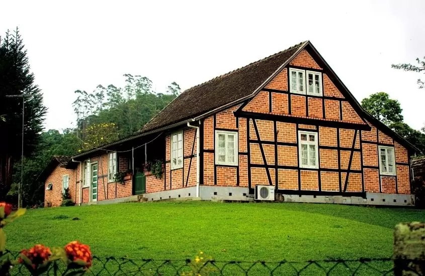 casa de tijolinhos vermelhos e telhado marrom, cercada por gramado verde em pomerode, durante o dia