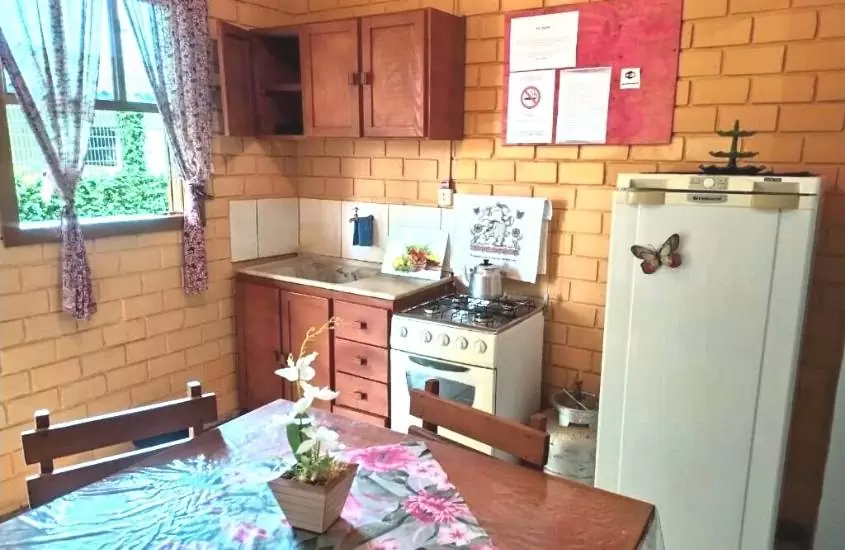 cadeiras e mesa de madeira, fogão e geladeira em cozinha de Pousada Cavalheiro
