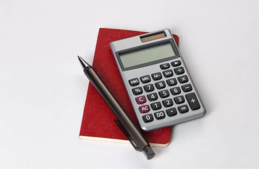vista de cima de caneta preta, calculadora e pequeno caderno vermelho em cima de mesa branca