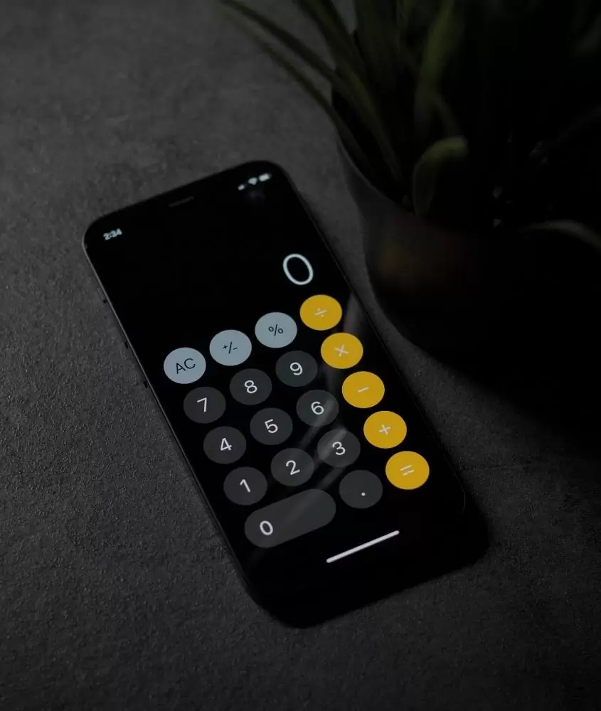 smartphone preto exibindo calculadora com número 0, em cima de mesa cinza