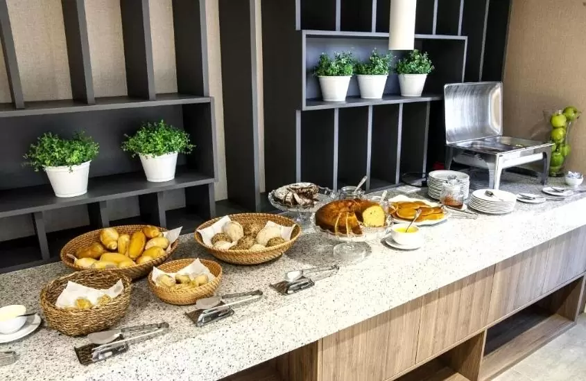 pães, bolos, pratos e talheres em cima de balcão de refeitório de Holiday Inn Express - Farroupilha, an IHG Hotel