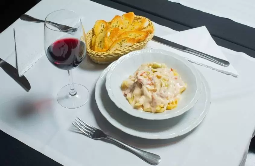 vista de cima de taça de vidro com vinho e massa dentro de prato branco em cima de mesa branca