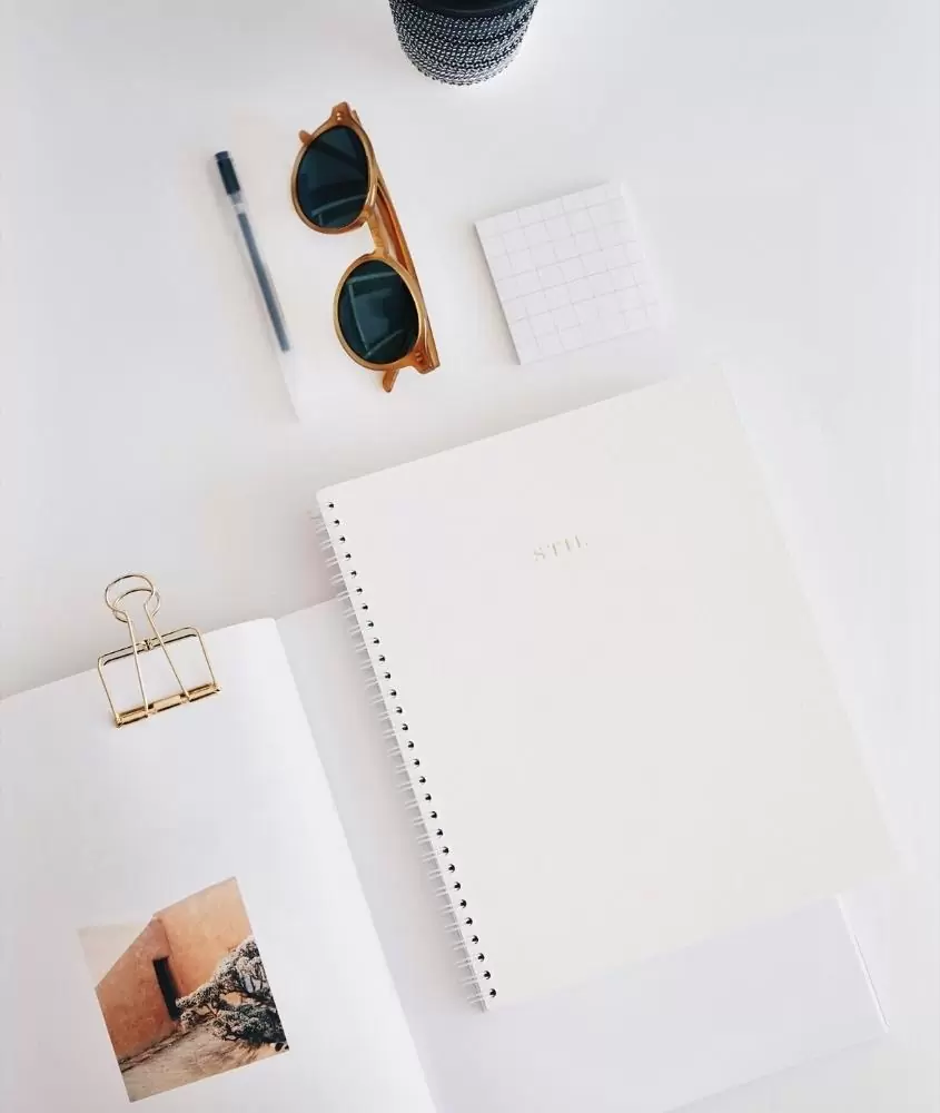 caderno de anotações, óculos de sol e caneta em cima de mesa branca