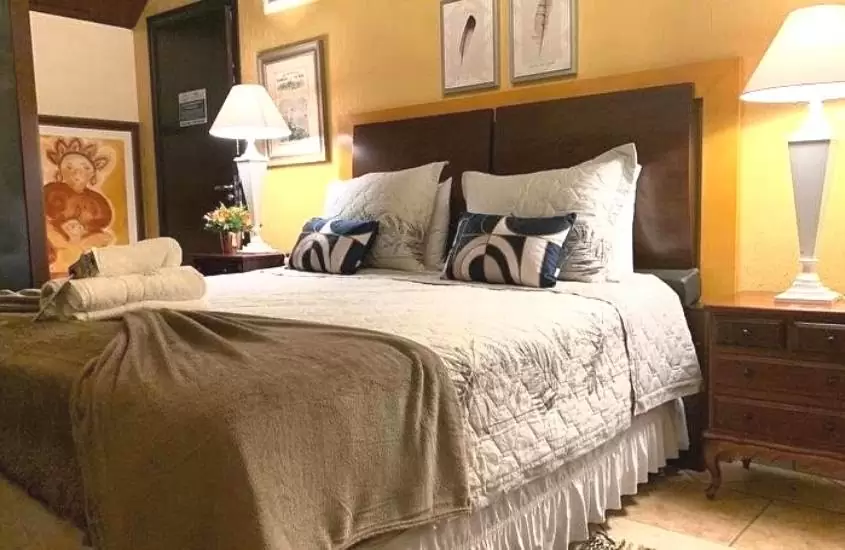travesseiros em cima de cama de casal e abajur em cima de móvel de cabeceira em suíte de VILLAGIO CHAPADA