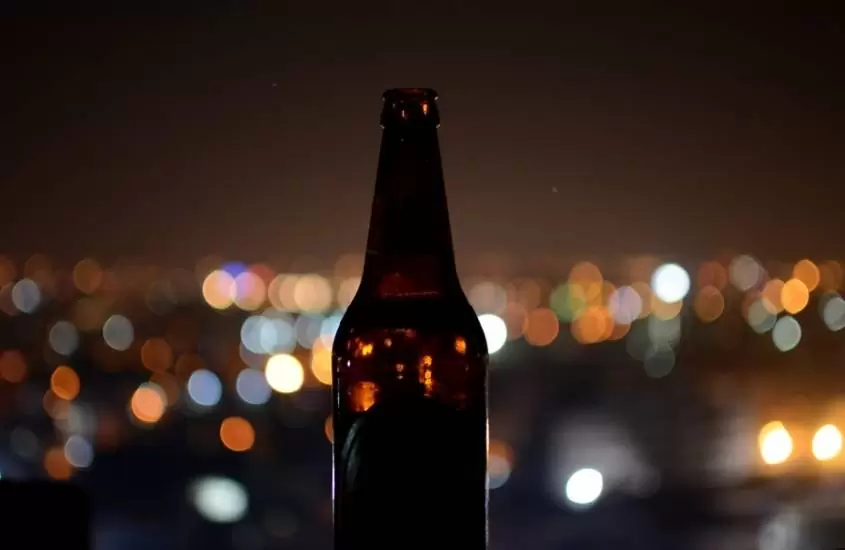 garrafa de vidro marrom de cerveja, ao fundo embaçado, luzes da cidade durante à noite