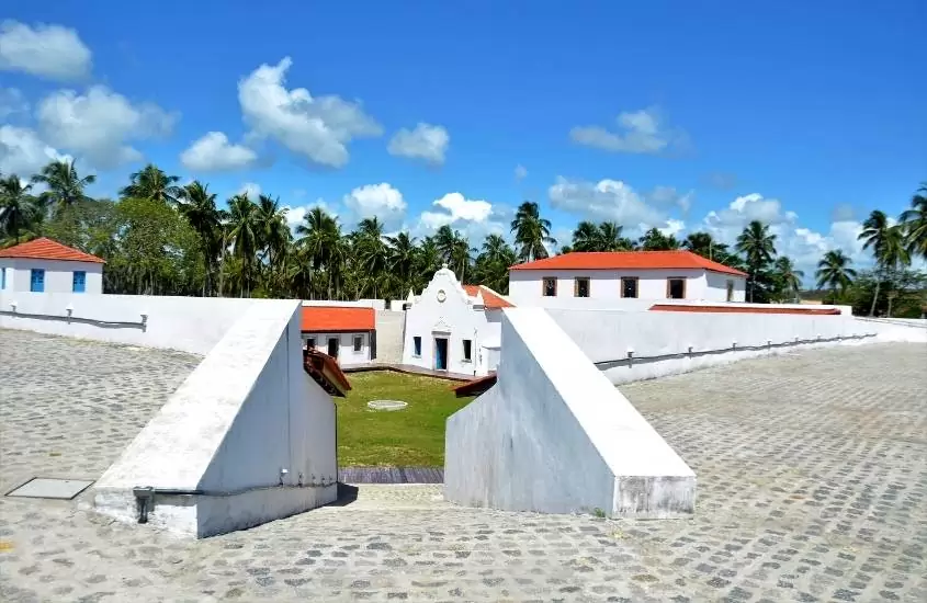 construções brancas com telhados vermelhos, rodeada de coqueiros em Forte de Santo Inácio de Loyola, durante dia ensolarado