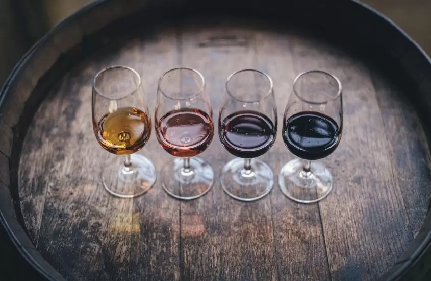 4 taças de vidro com diferentes vinhos em cima de barril de madeira