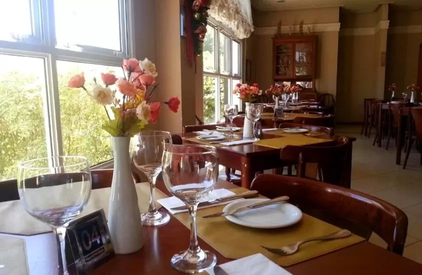 taças de vidro, talheres em cima de prato branco e vaso com flores em cima de mesa de restaurante de Hotel Villa Michelon