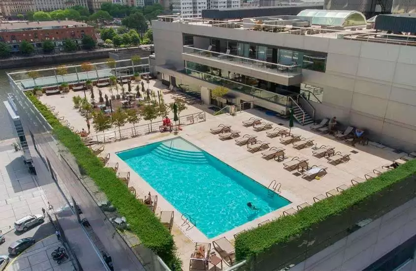 Em um dia de sol, vista aérea de área de lazer de hotel com piscina, espreguiçadeiras e plantas ao redor