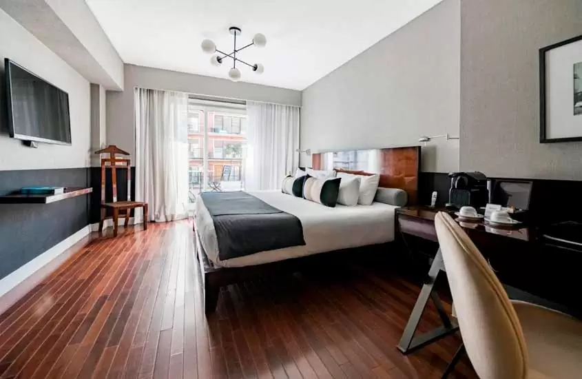 Quarto de um dos melhores hotéis de Buenos Aires com cama de casal, mesa de trabalho com cadeira, cafeteira elétrica, quadro decorativo, TV e janela grande acortinada