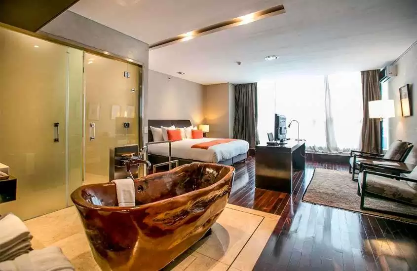 Quarto de um dos melhores hotéis em Buenos Aires com banheira de madeira, cama de casal, poltronas, tapetes, TV, janelas grandes acortinadas e quadros decorativos