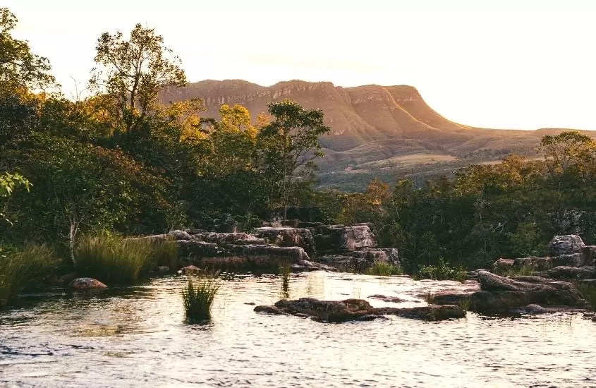 piscina natural cercada de árvores e formações rochosas ao fundo, durante entardecer em chapada dos veadeiros