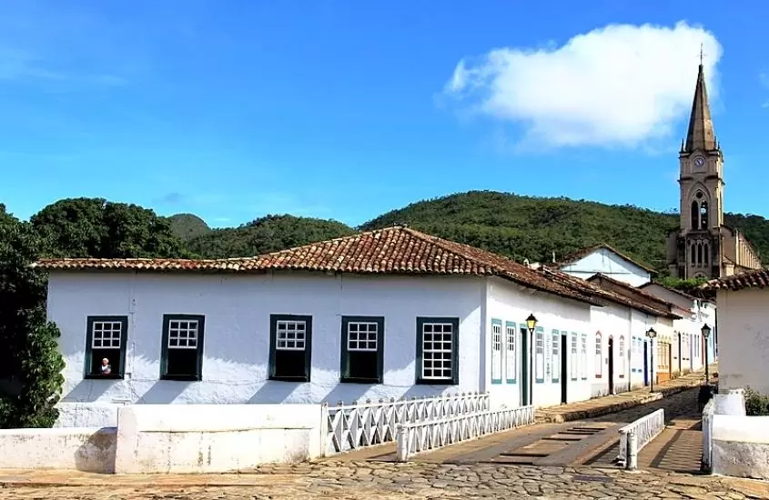 durante o dia, casa branca com diversas janelas amplas azuis, e igreja e ao fundo igreja e montanhas