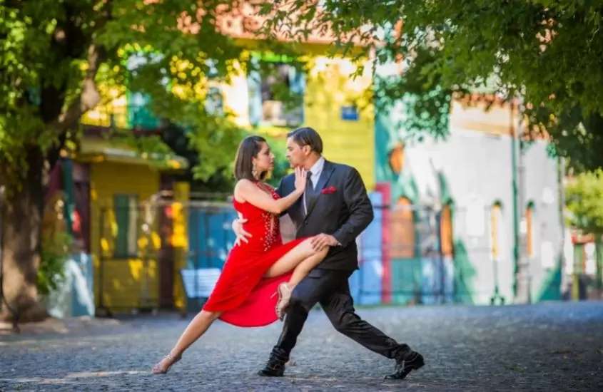 mulher com vestido vermelho e homem com terno preto, dançam tango em rua de buenos aires, durante o dia