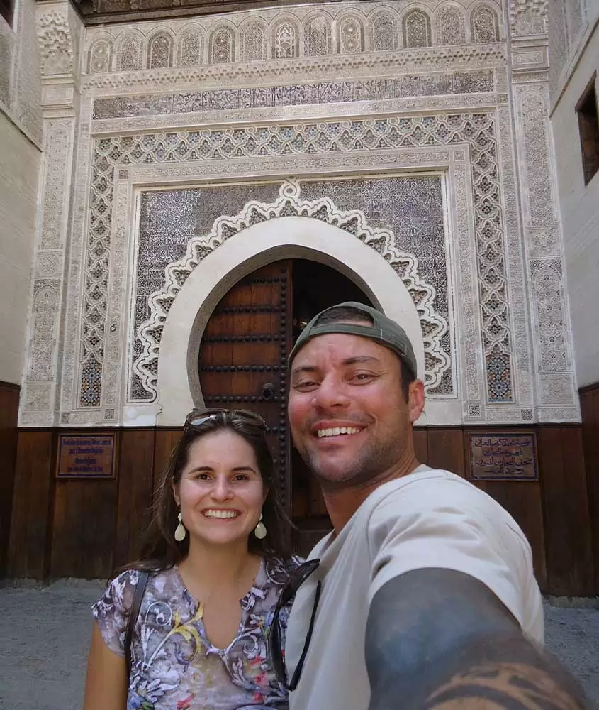 barbara rocha com camisa estampada e vagner alcantelado com boné verde e blusa branca; ambos sorriem para foto em frente a uma medina, um dos melhores passeios marrocos