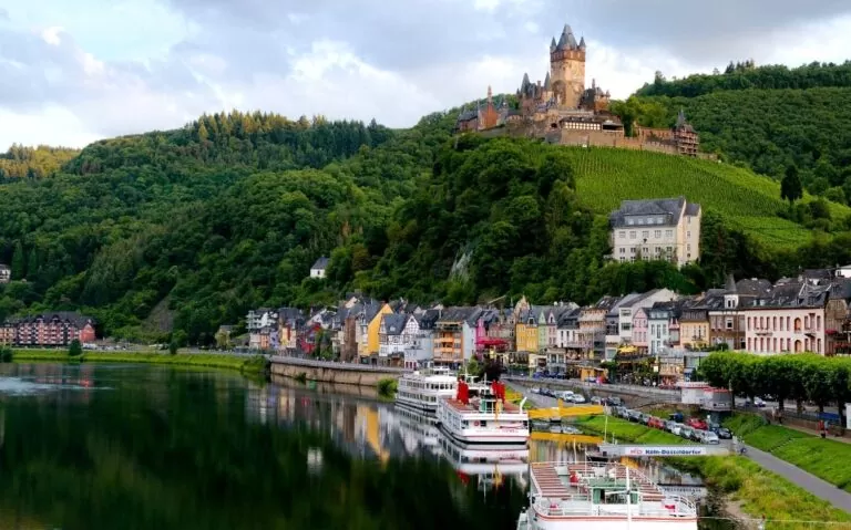 durante o dia, castelo em topo de montanha, e casas coloridas abaixo à beira de lago em uma das cidades da alemanha para visitar
