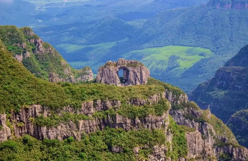 vista aérea de formação rochosa com furo no meio e montanhas ao fundo, em um dos pontos turísticos na serra catarinense