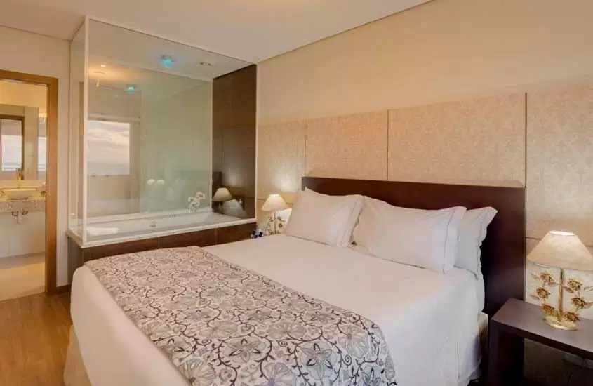 banheira de hidromassagem, cama de casal e mesa da cabeceira em suíte de um dos melhores hoteis em porto alegre