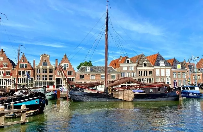 durante o dia, barcos atracados em lago em frente a diversas casas de tijolos vermelhos em hoorn, destino para o Roteiro Holanda