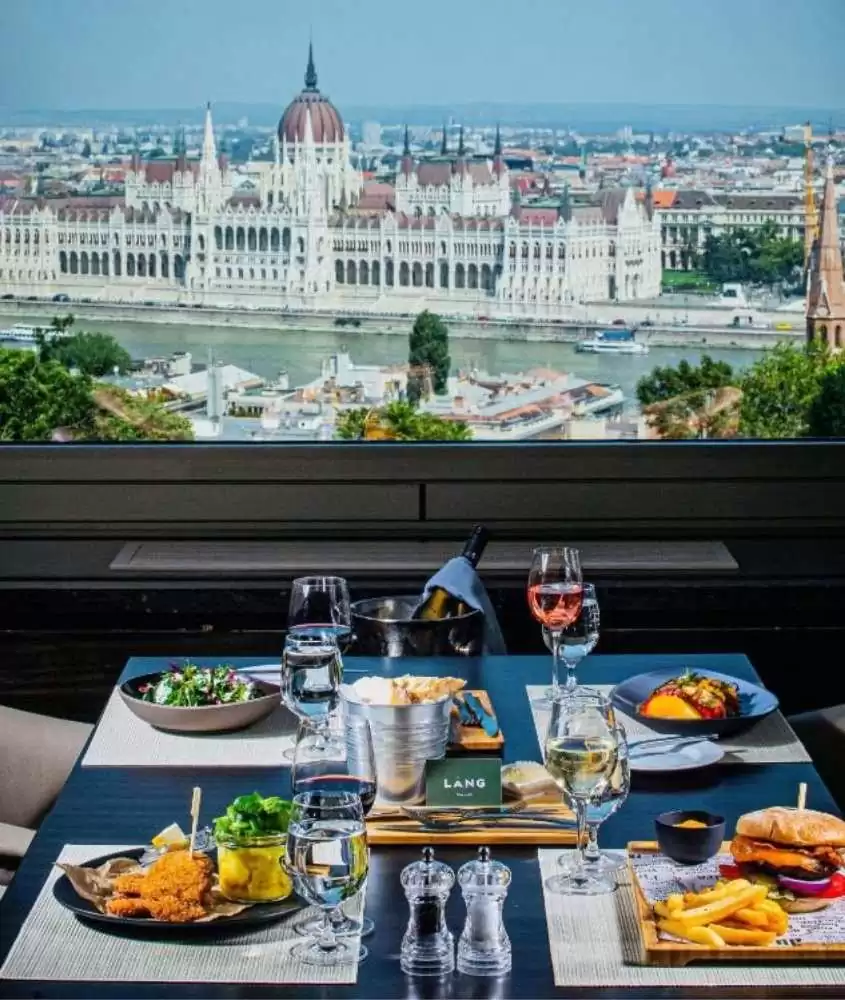 hambúrguer, batata frita, frango, saladas e taças de vidro em mesa de restaurante de hotel em bucareste com ampla vista para o rio danúbio